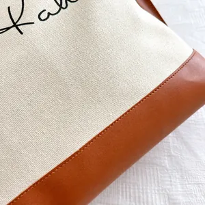 Détail du cabas en toile avec couture en cuir marron et lettres brodées noires