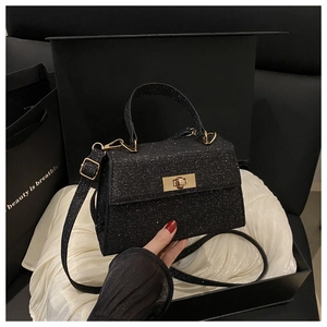 Detailed close-up of a black glitter handbag with a gold twist lock on silk padding