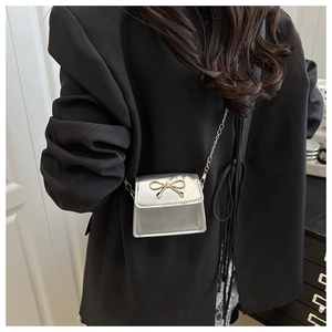 Close-up of mini silver crossbody bag with gold bow clasp worn on black blazer