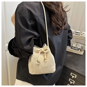 Dettaglio di una borsa a secchiello intrecciata in paglia beige con coulisse e tracolla