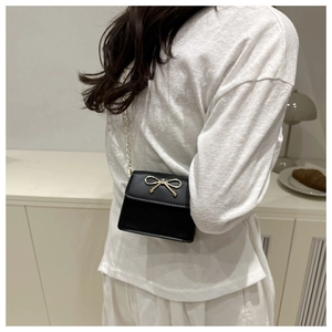 Close-up of small black crossbody bag with golden bow hardware and chain strap