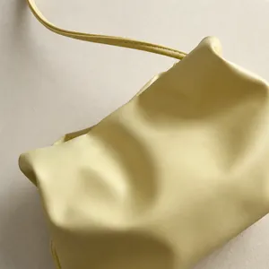 Close-up of soft yellow cloud bag showing gathered leather texture and pearl strap detail