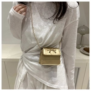 Golden mini crossbody bag with metal bow detail and elegant chain strap on a model