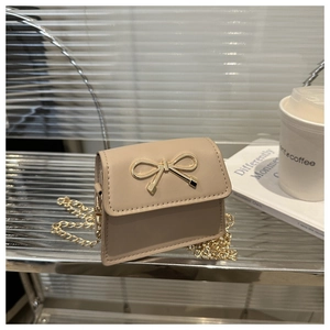 Detail of a beige mini crossbody bag featuring a golden bow buckle and slim chain strap