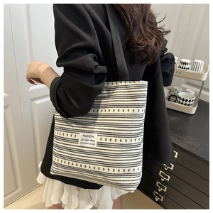 Détail d'un sac cabas en toile rayée avec sangle noire montrant le tissu texturé