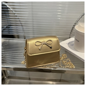 Detail of a mini gold crossbody bag featuring a metal bow clasp and fine chain strap