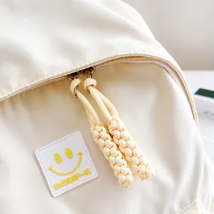Primer plano de mochila de nailon beige con parche de cara sonriente y cremalleras tejidas