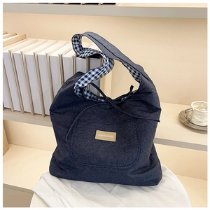 Detail van blauwe denim draagtas met geruite voering en modelabel op houten plank