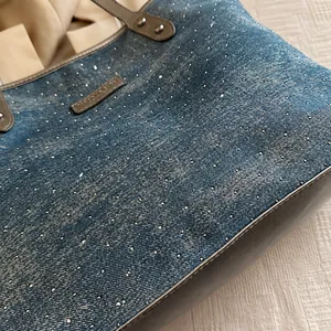 Close-up of light blue denim tote with sparkling silver rhinestones and leather handles