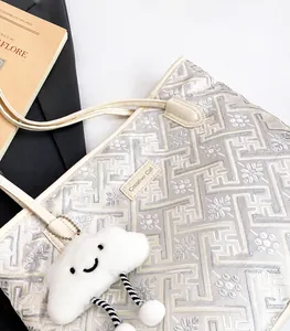 Close-up of beige tote bag featuring floral embroidery, Creative Cat label and cloud charm