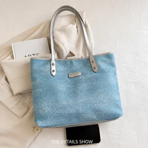 Close-up of light blue denim tote bag with subtle glitter finish and silver metal straps