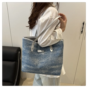 Detail of blue denim tote bag with gray leather strap and fashion metal logo tag