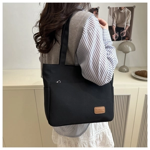 Detalle del bolso tote de lona negra con el bolsillo frontal y el parche de cuero