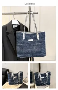 Close-up of deep blue denim tote bag with silver handles and front metal logo detail