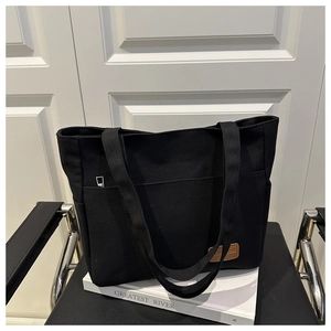 Detalle de bolso tote de lona negra con parche de cuero marrón y cremallera plateada