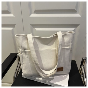 Detalle de bolso tote de lona blanca con bolsillo de cremallera y logo de cuero