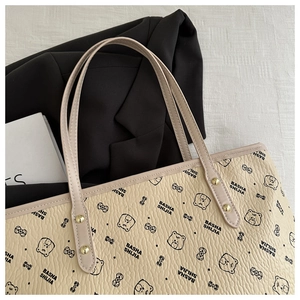 Macro detail of beige faux leather tote bag with cartoon bear prints and gold rivets
