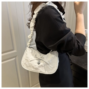 Detalle del bordado floral en bolso blanco de hombro con colgante de corazón plateado