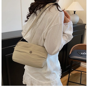 Detail of a beige quilted crossbody bag with metal emblem shown on a model