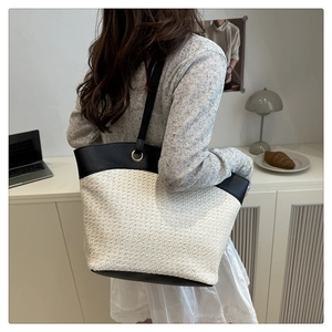 Straw tote bag with black leather trim and gold eyelets shown on a shoulder