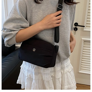 Detail view of black quilted crossbody bag with metal M logo and wide strap on model