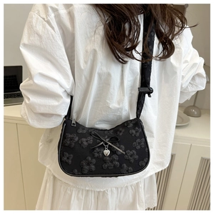 Detalle de textura floral en bolso negro con colgante de corazón usado por modelo