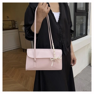 Detailansicht der rosa Schultertasche mit einer zarten weißen Schleife am Riemen
