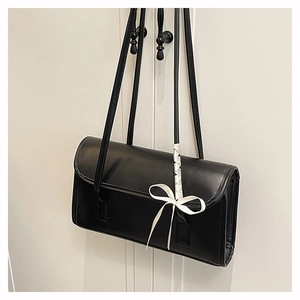 Detalle de bolso baguette negro con elegante lazo de cinta blanca en la bandolera