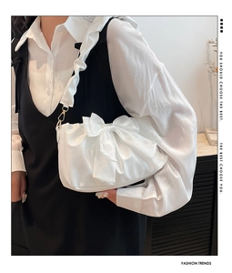 Witte geplooide cloud bag met grote strik en gouden ketting gedragen door model