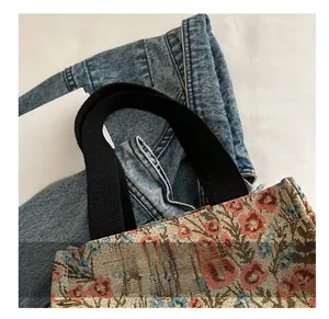 Detail of floral jacquard tote bag with black canvas handle and beige fabric texture