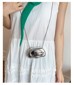 Détail du sac en métal argenté brillant avec design annulaire et fine chaîne argentée