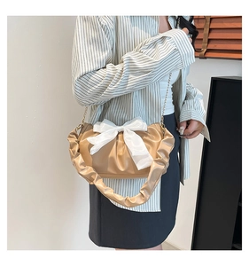 Detail van kaki geplooide handtas met grote witte zijden strik en metalen ketting