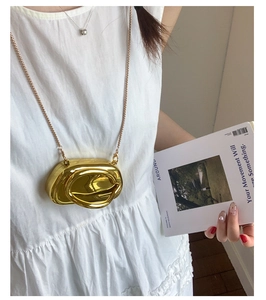 Détail d'un mini sac boîte doré avec fine chaîne sur un mannequin en robe blanche chic