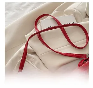 Detail showing the adjustable shoulder strap and silver buckle of the red glossy bag
