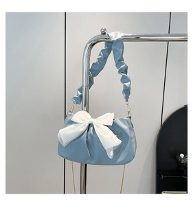 Detail van lichtblauwe geplooide handtas met grote witte strik en gouden ketting