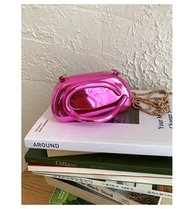 Détail du mini sac métallique rose avec chaîne à billes dorée posé sur des livres