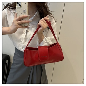 Detail of red patent leather underarm bag featuring a magnetic flap and brand embossing