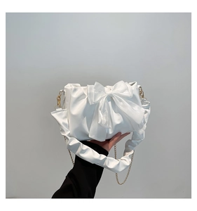Detail van witte geplooide handtas met grote organza strik en gouden kettingriem