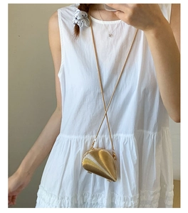 Close-up of golden shell evening bag with ribbed texture on a white summer dress
