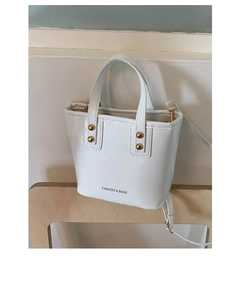 Detail of white bucket bag with gold studs and adjustable strap on a wood chair