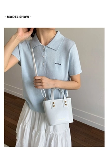 Close-up of a white bucket bag with gold studs and a slim strap held by a model