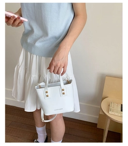 Close-up of elegant white bucket bag featuring gold rivets and detachable shoulder strap