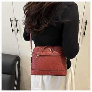 Detail of burgundy shell-shaped crossbody bag featuring woven leather texture and double zippers