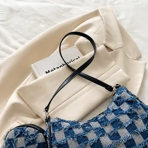 Detail of checkered denim crescent bag with frayed edges and slim black leather strap