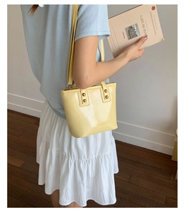 Close-up of creamy yellow bucket bag with glossy finish and elegant gold hardware
