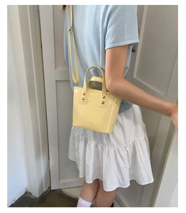 Macro shot of yellow patent leather bucket bag with gold rivets and shoulder strap