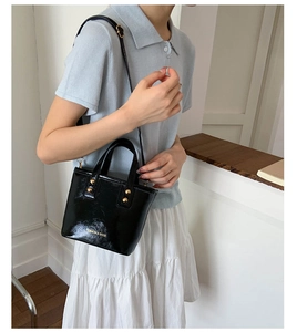 Detail of black glossy mini bucket bag with gold studs and adjustable shoulder strap