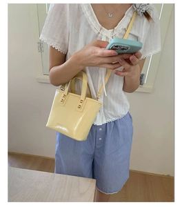 Detail of pale yellow patent leather bucket bag featuring gold cylindrical accents