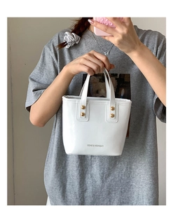 White glossy patent leather mini tote bag detail with gold rivets and front text logo