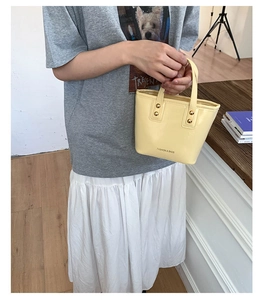 Detail of yellow mini bucket bag with gold rivets and black fashion lettering